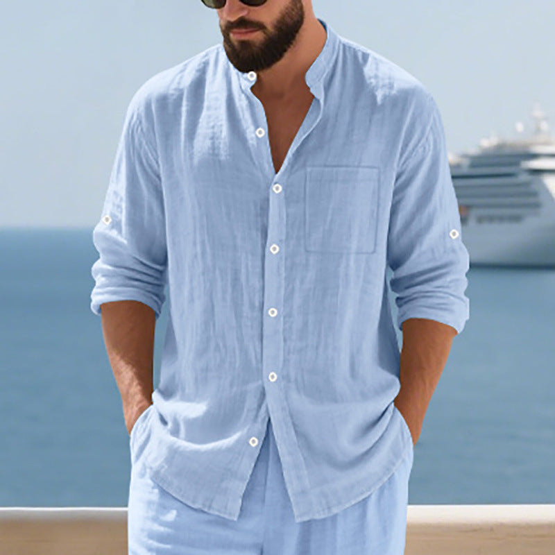 Man wearing a light blue shirt and pants with a blurred background of water and a ship.