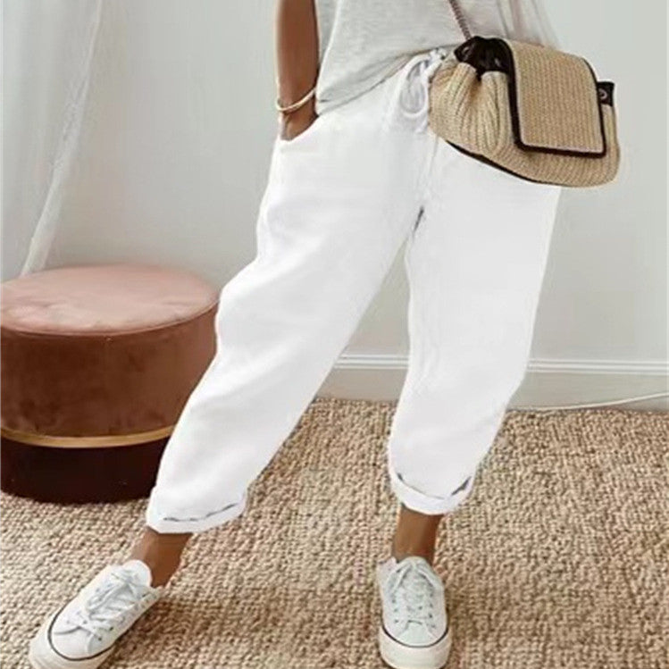 Person wearing white pants and sneakers with a straw bag indoors.