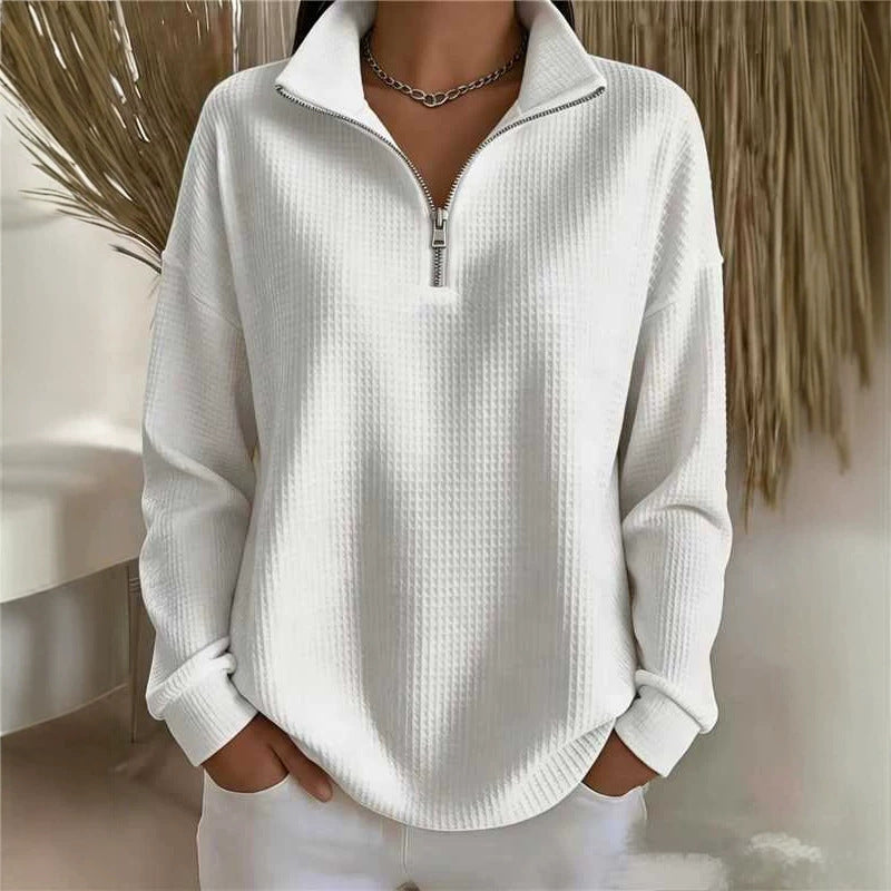A woman wearing a white waffle-knit long-sleeve quarter-zip pullover sweater with a stand collar, paired with white pants and a silver chain necklace.