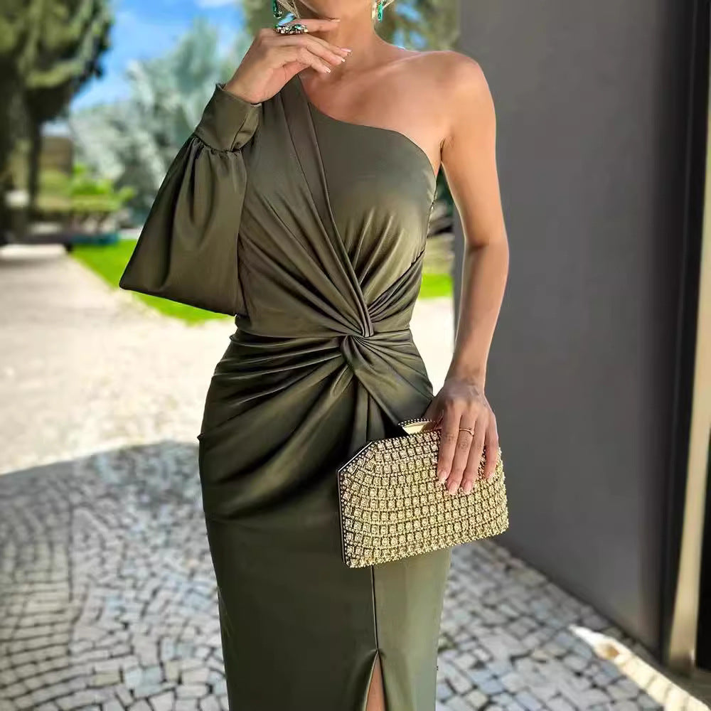 Woman in an olive green one-shoulder dress holding a gold clutch outdoors.