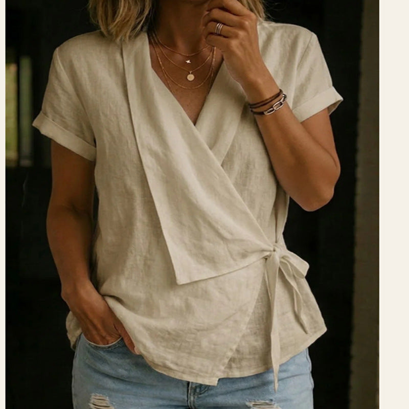 Woman wearing a light-colored top with a tie detail and denim shorts against a dark background