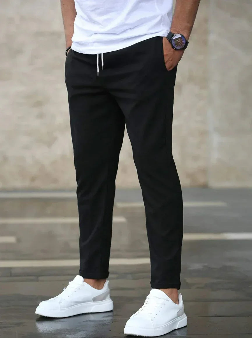 Person wearing black pants and white sneakers against a neutral background