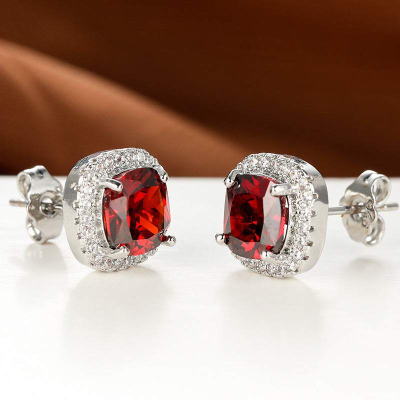 Pair of red gemstone earrings with silver setting on a white surface.