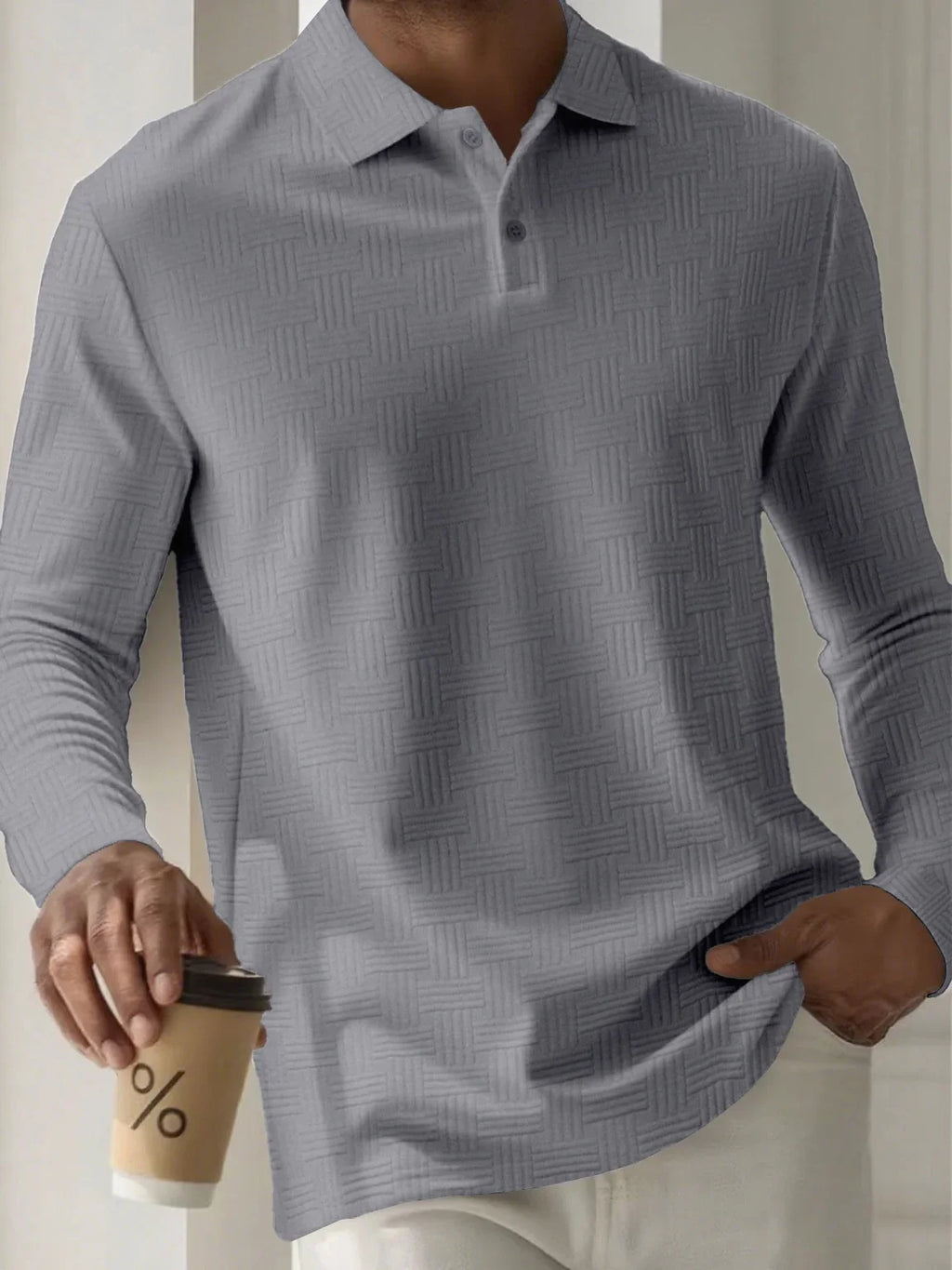 Person wearing a gray patterned shirt holding a coffee cup.