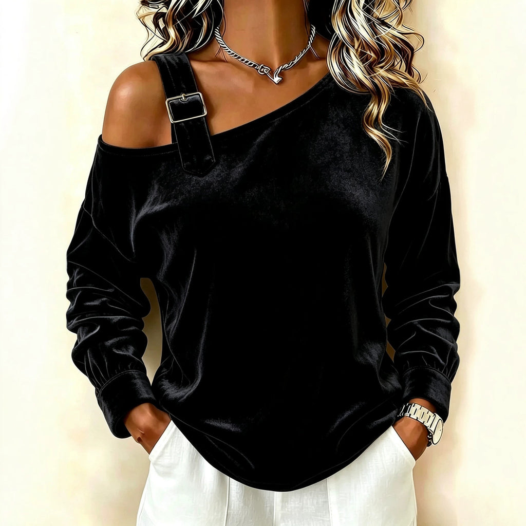 A woman wearing a black velvet one-shoulder cold-shoulder top with a decorative strap and buckle detail on the shoulder, paired with white pants.