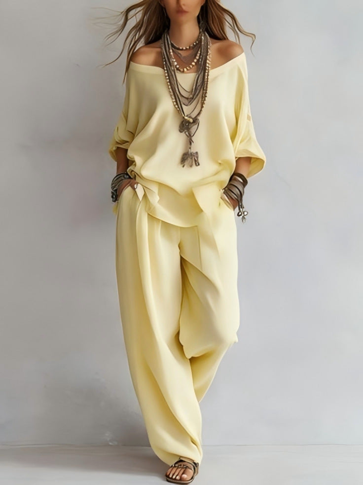 Person wearing a light yellow outfit with layered necklaces on a plain background