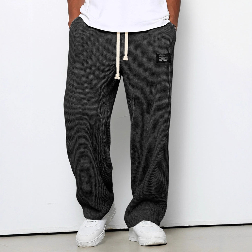 Person wearing black checkered pants with a white label on a plain background
