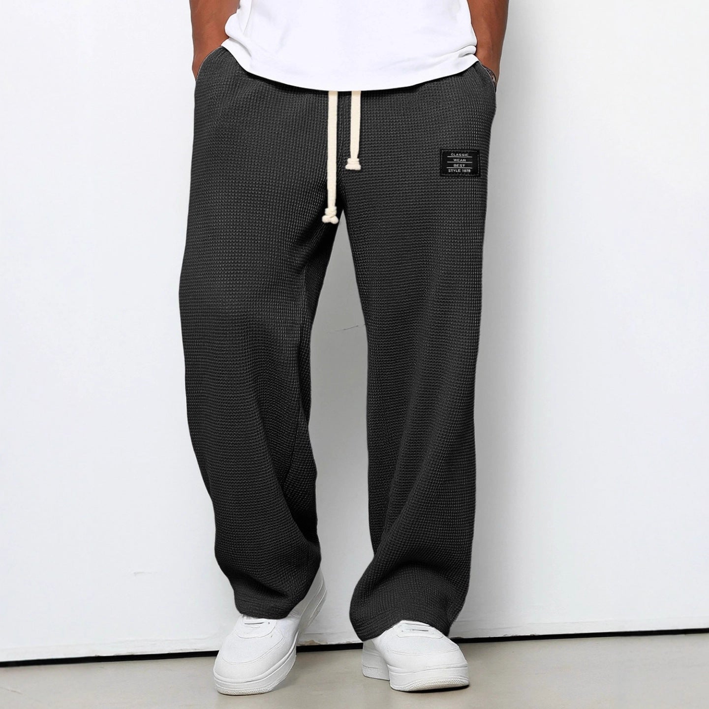Person wearing black checkered pants with a white label on a plain background