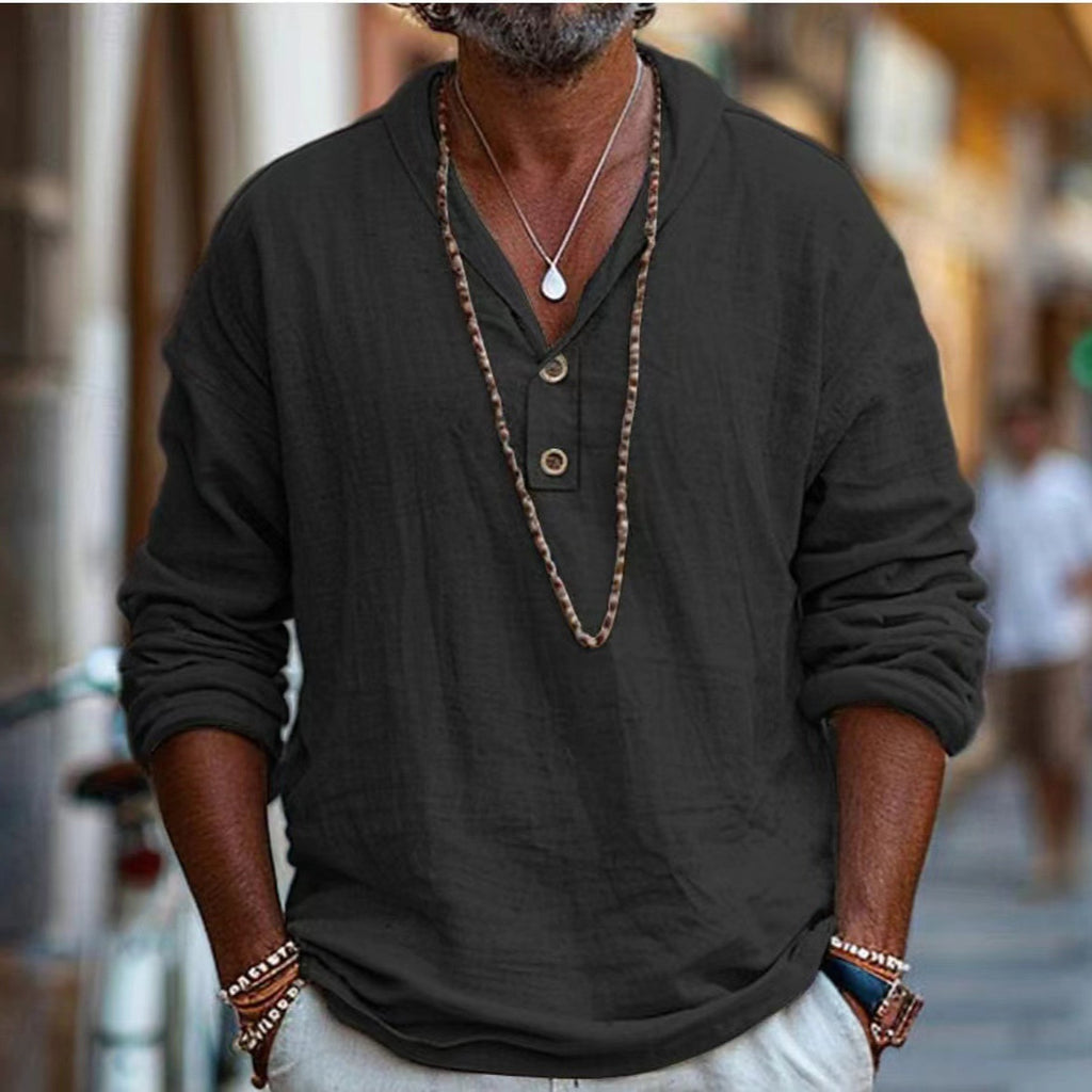 Man wearing a dark long-sleeve shirt with buttons, necklace, and bracelets in an urban setting.