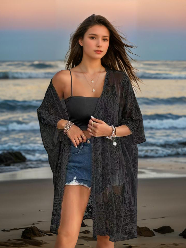 Woman standing on a beach wearing a black kimono-style garment, denim shorts, and a black top.