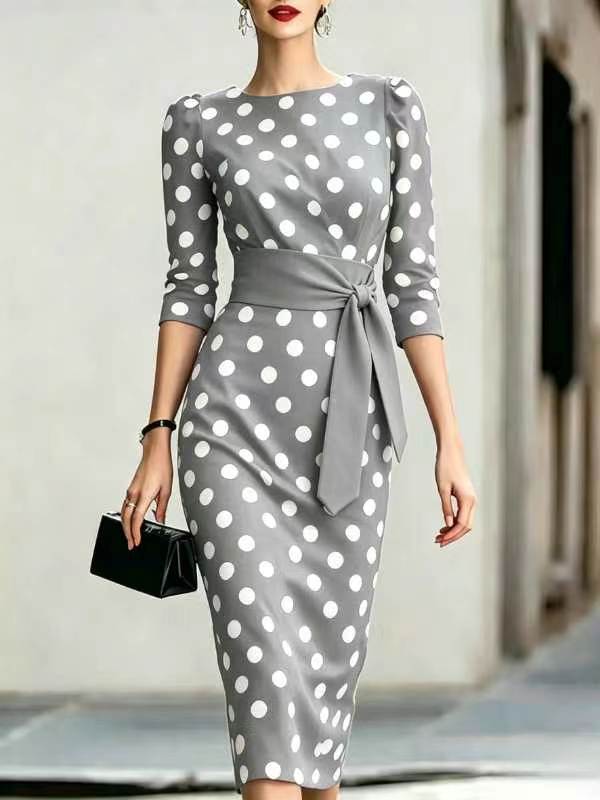 Woman wearing a gray dress with white polka dots, holding a black clutch.