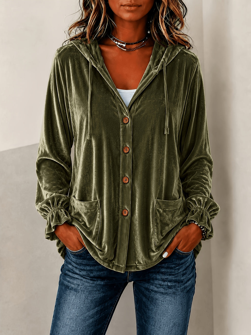 A woman wearing an olive green velvet hooded button-up shirt with drawstrings and front pockets, paired with blue jeans.