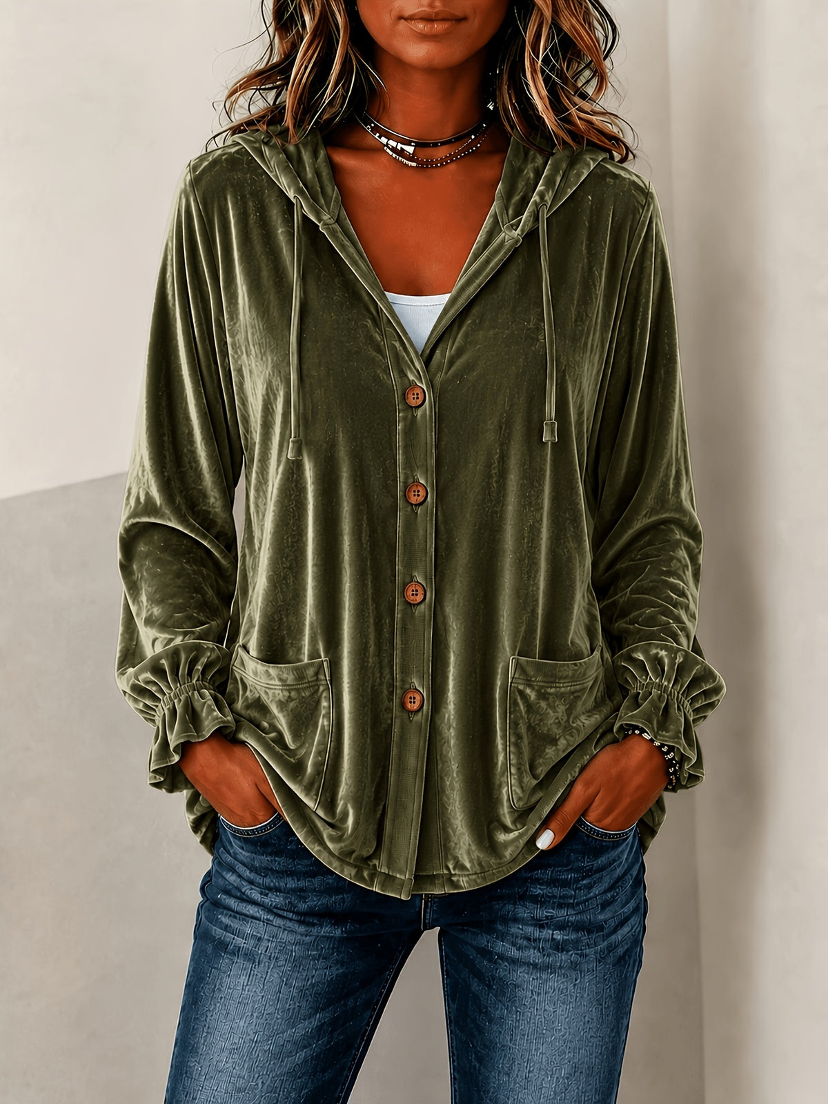 A woman wearing an olive green velvet hooded button-up shirt with drawstrings and front pockets, paired with blue jeans.