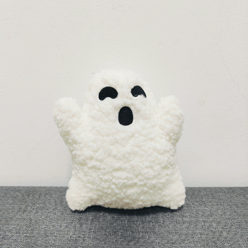 White ghost-shaped pillow with black eyes and mouth on a gray surface.