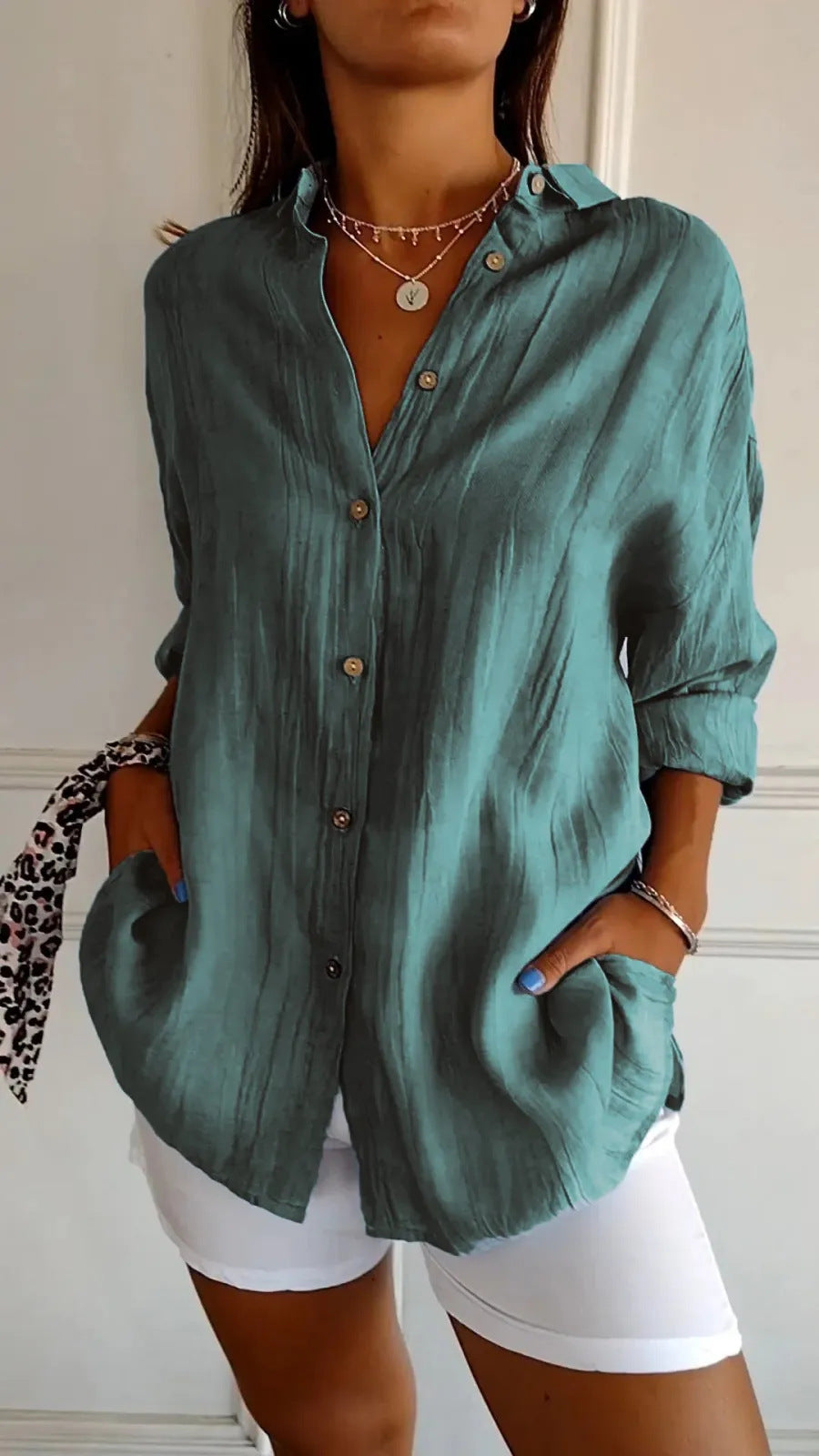 Person wearing a teal button-up shirt with white shorts indoors.