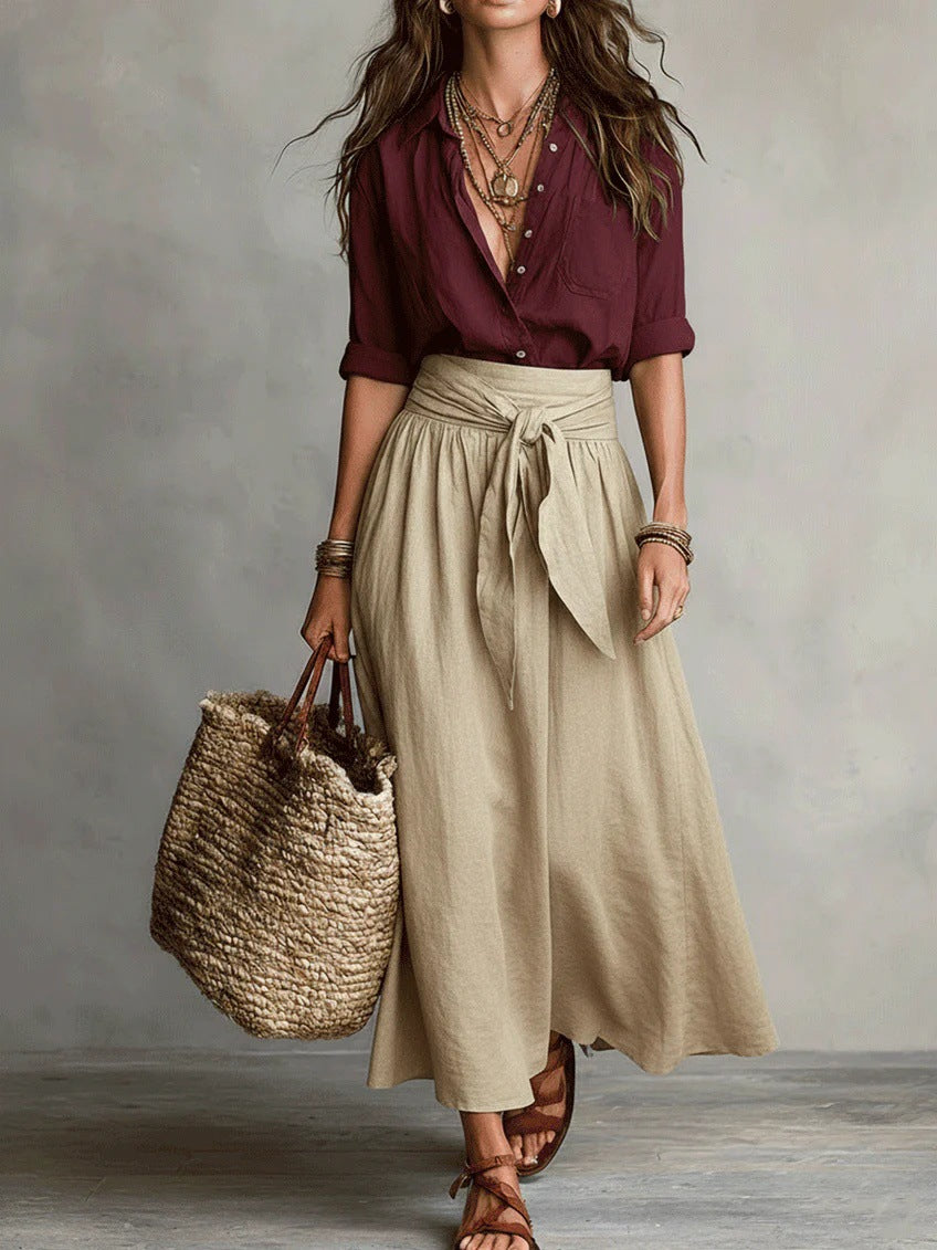 Woman wearing a burgundy blouse and beige skirt, holding a woven bag against a neutral background