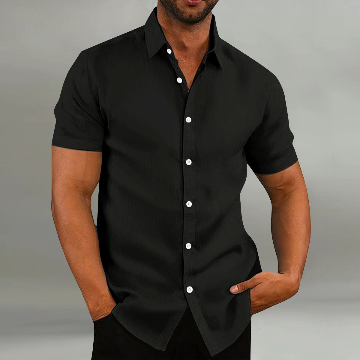 Man wearing a black short-sleeve shirt with white buttons on a gray background
