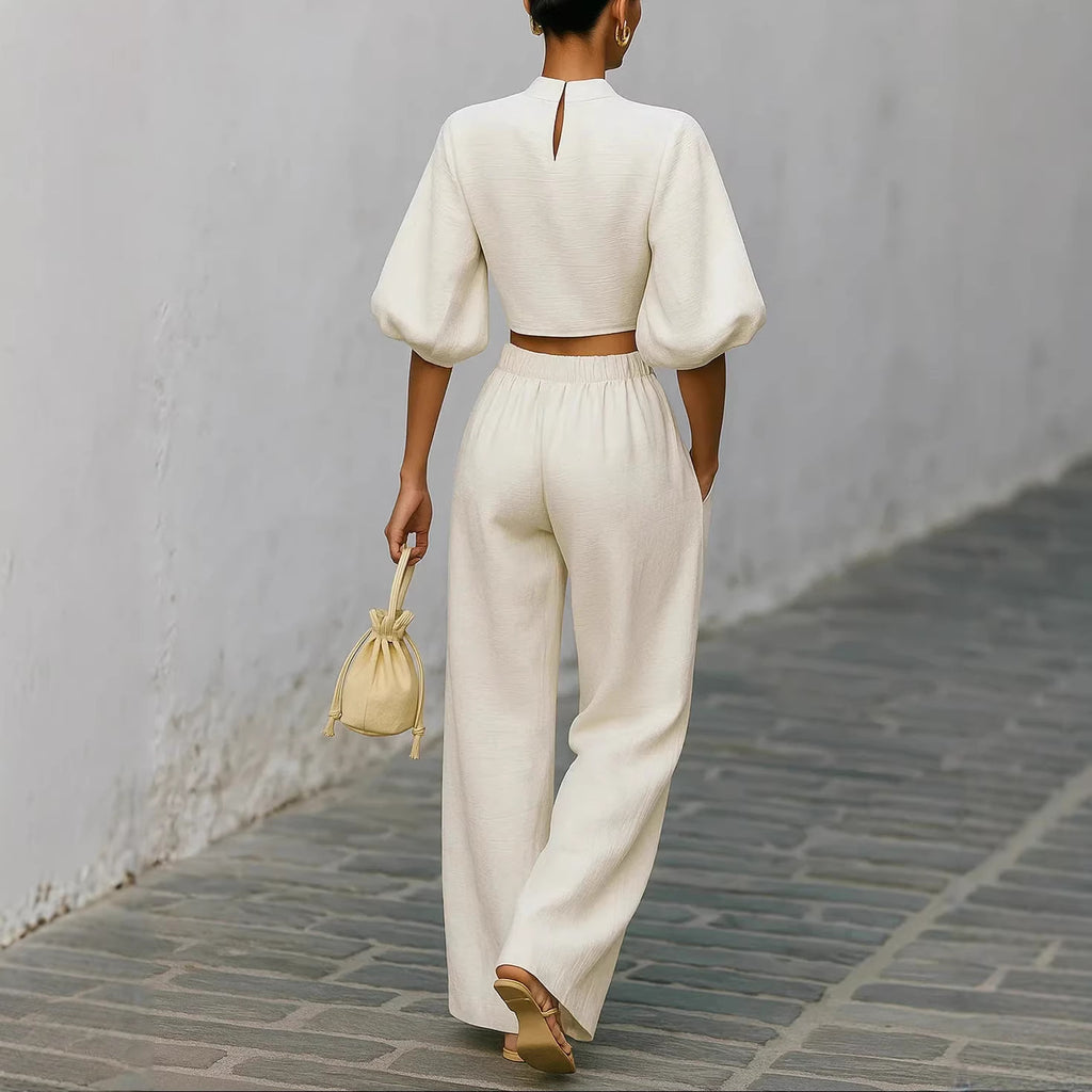 Person wearing a white outfit walking on a gray pavement with a light-colored wall in the background.