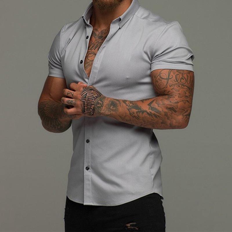Man wearing a light gray short-sleeve shirt with tattoos on arms against a gray background
