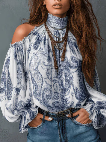 A woman wearing a white cold-shoulder blouse with a blue paisley pattern, paired with blue jeans and layered brown necklaces, set against a dark gray background.