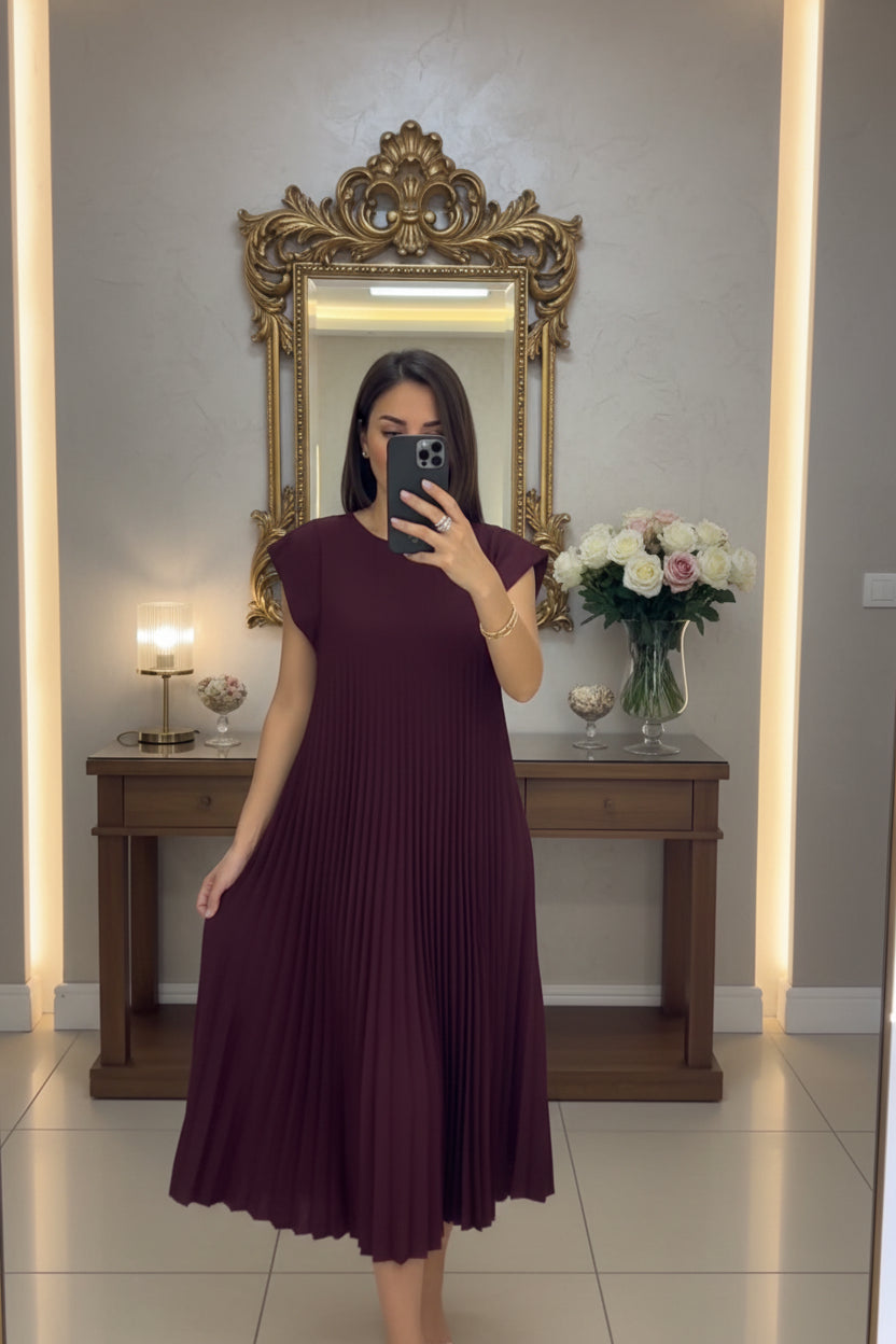 Person wearing a burgundy pleated dress in a room with decor elements.