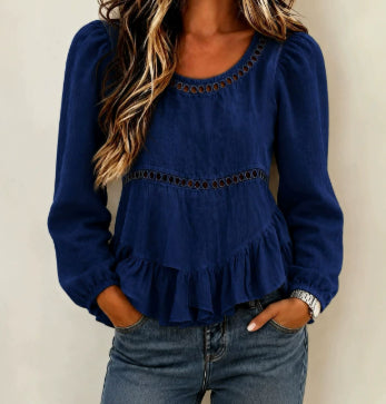 A woman wearing a navy blue long-sleeve blouse with puff sleeves, a scoop neckline, and decorative eyelet lace trim, paired with blue jeans.