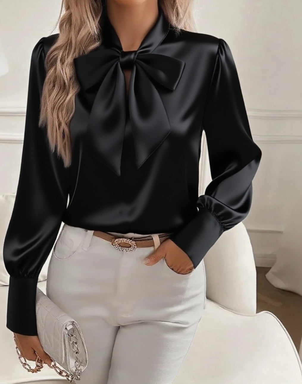 Black satin blouse with a large bow tie worn by a person sitting on a white chair.