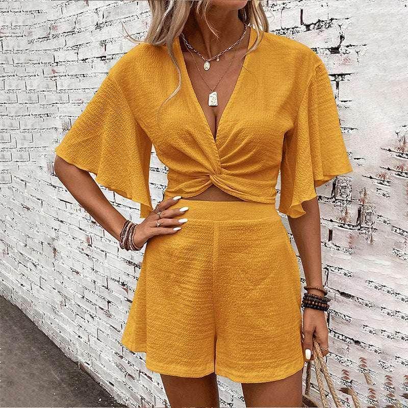 Woman wearing a yellow short-sleeve two-piece outfit by ZA-Zola, standing by a white brick wall