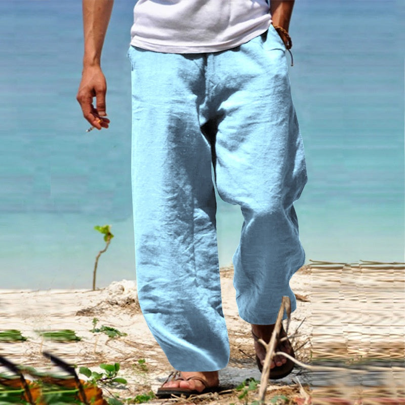 Person wearing light blue pants and a white shirt standing on a beach with ocean in the background