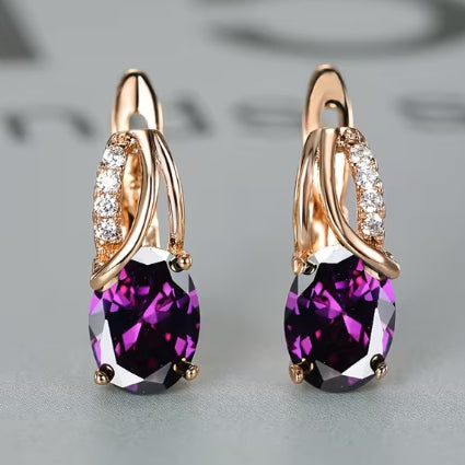 Pair of earrings with purple gemstones and rose gold accents on a light gray background