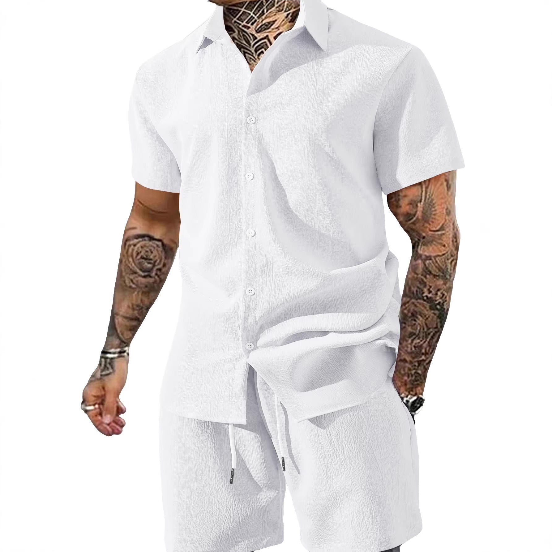 Man wearing a white button-up shirt and shorts set with tattoos on arms.