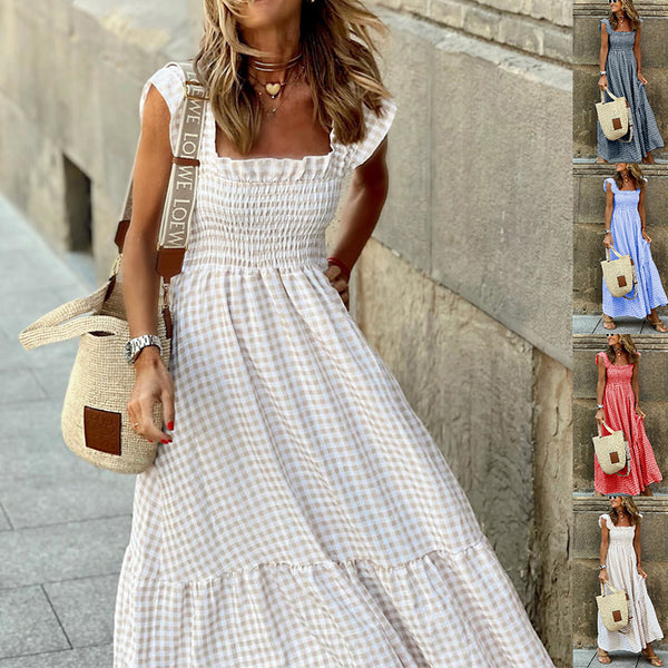 Woman wearing a white checkered dress with a straw bag, standing against a stone wall.