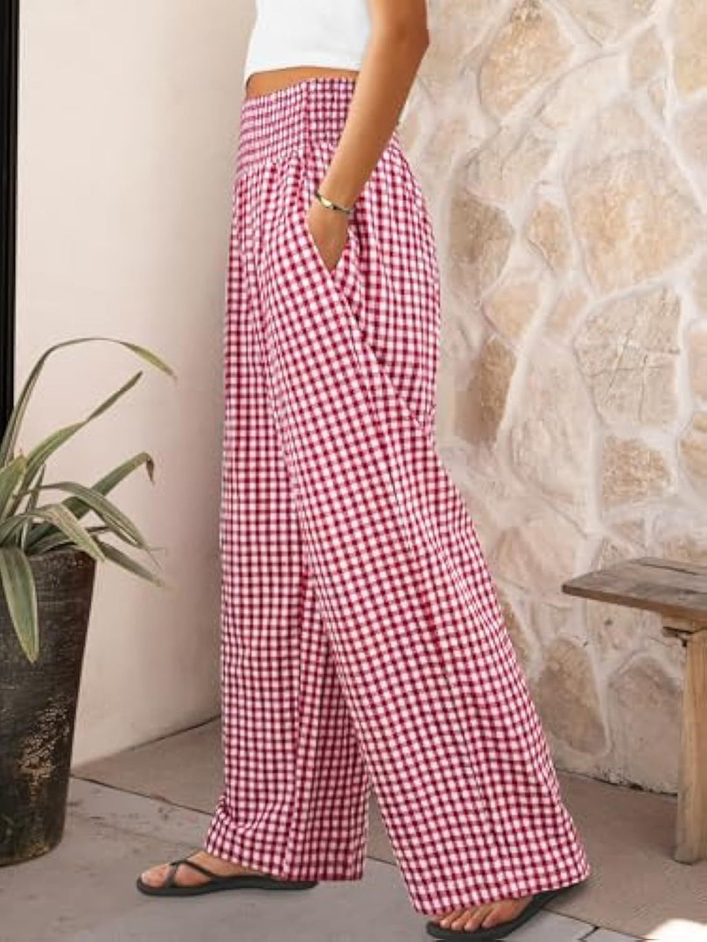 Person wearing red and white checkered pants standing against a stone wall.