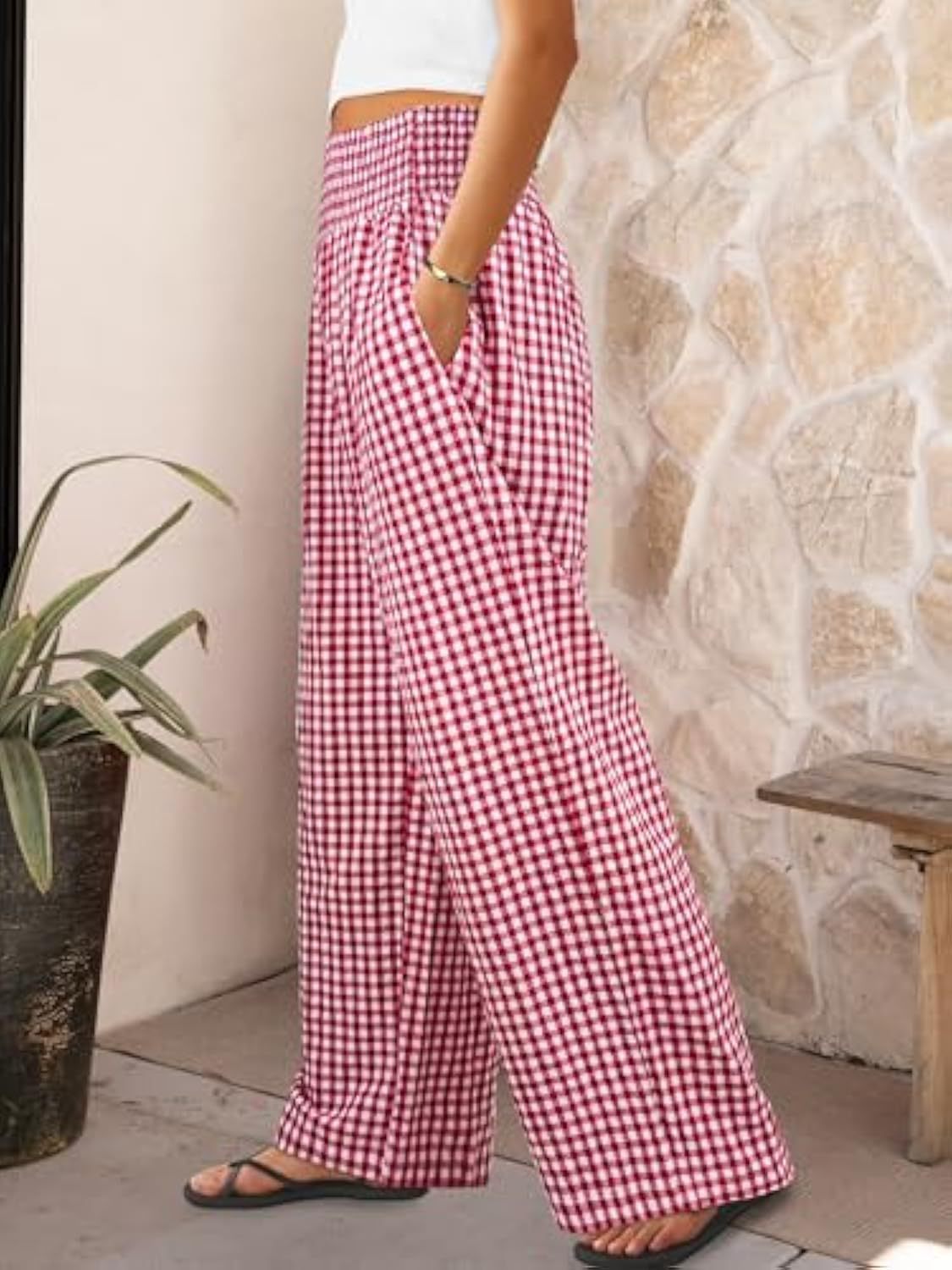 Person wearing red and white checkered pants standing against a stone wall.