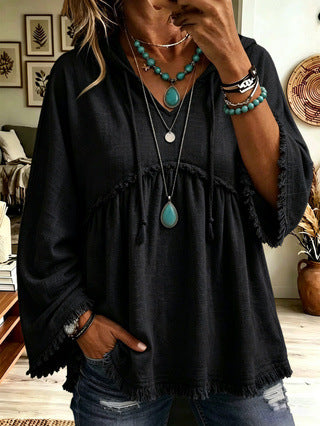 A woman wearing a loose black bohemian-style blouse with fringed edges and drawstring details, paired with distressed blue jeans and layered turquoise and silver necklaces.
