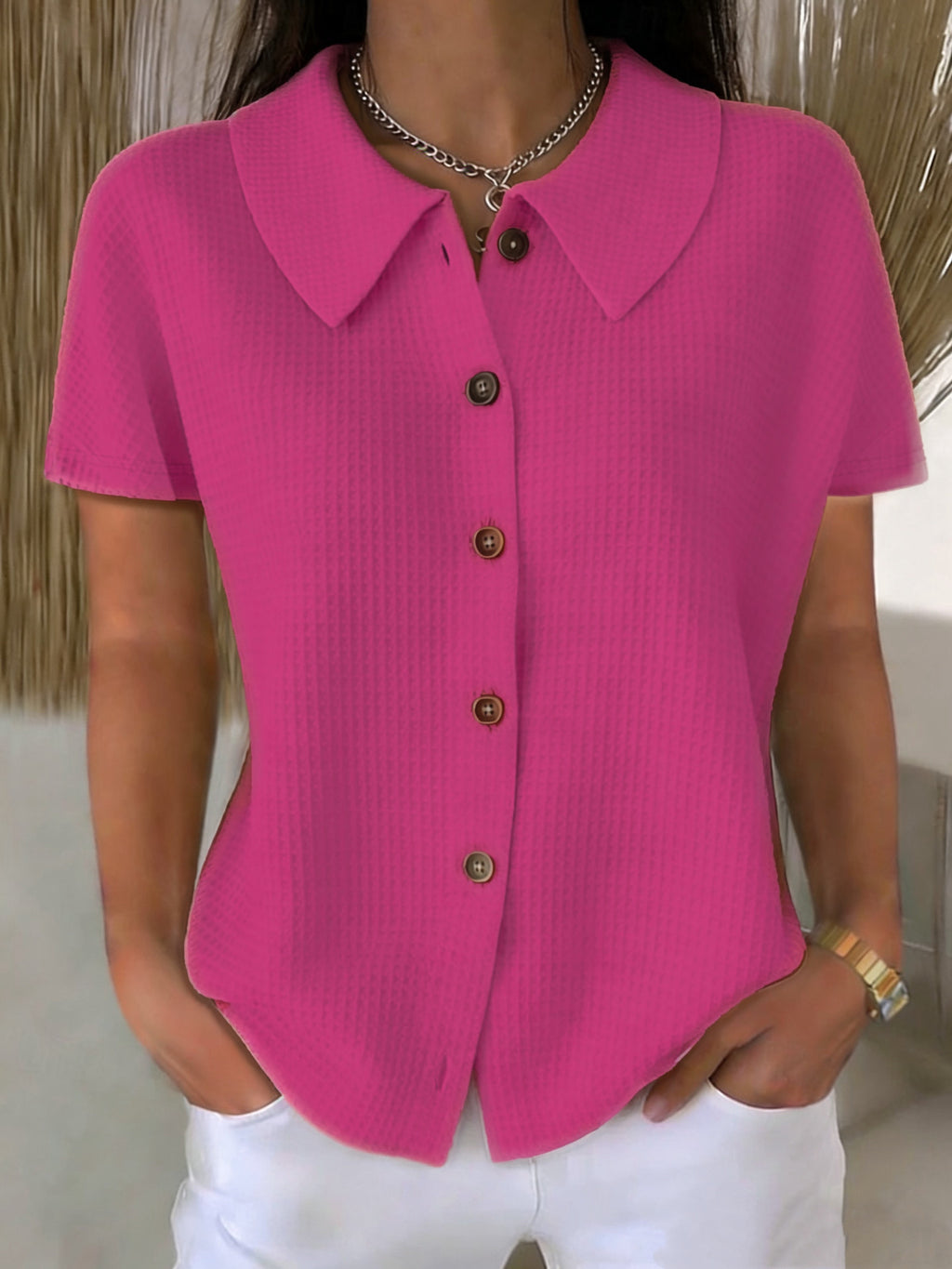 Person wearing a bright pink short-sleeve blouse with buttons, standing against a neutral background.