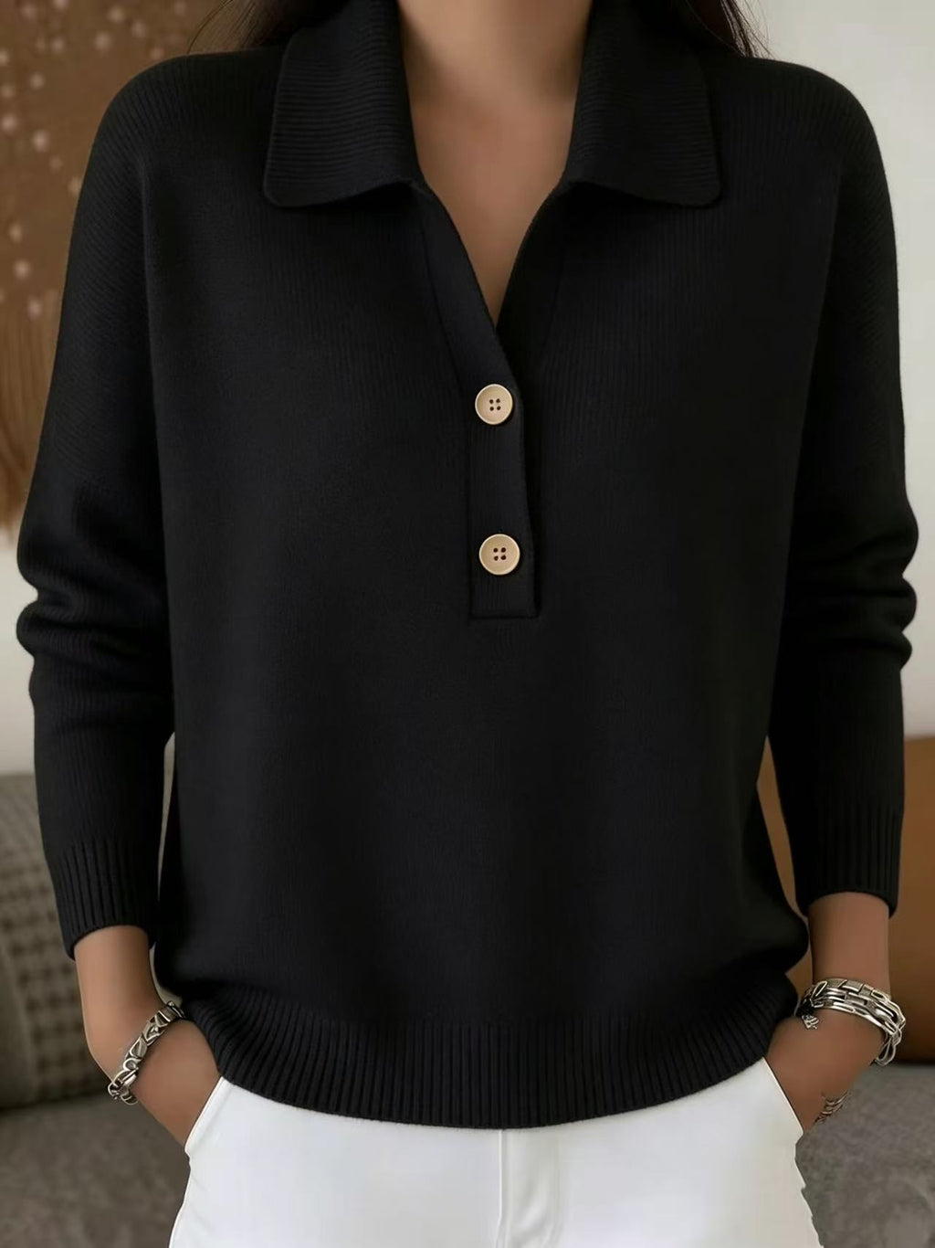 Person wearing a black sweater with gold buttons against a neutral background
