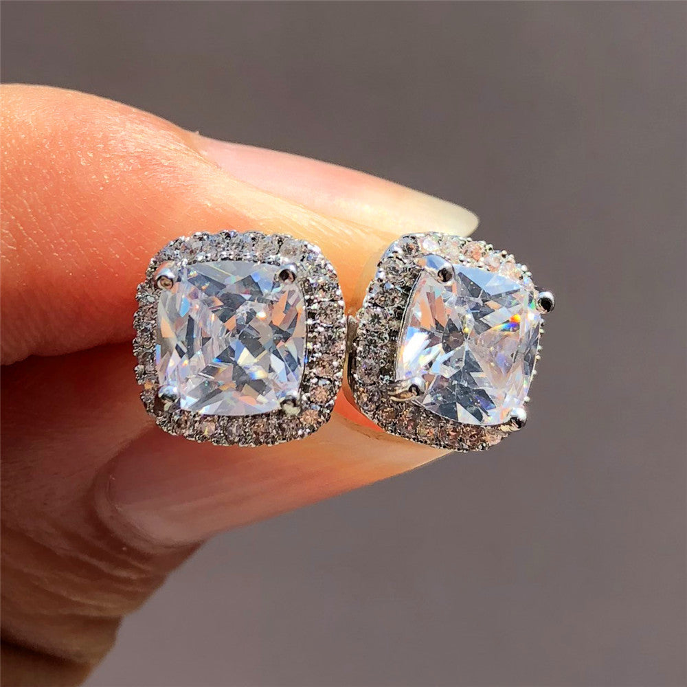 Diamond earrings held between fingers against a neutral background