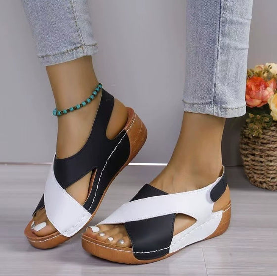 Black and white sandals with brown soles worn by a person on a neutral background