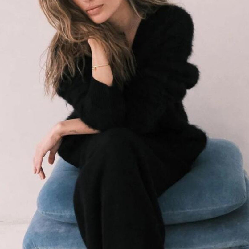 Person wearing a black outfit sitting on a blue cushion against a light background