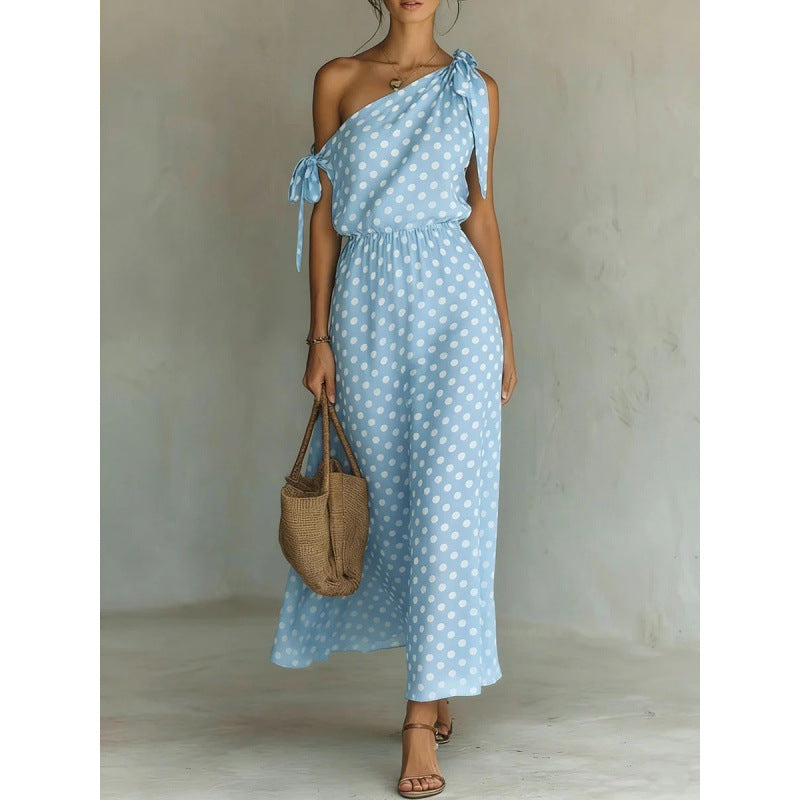 Woman wearing a light blue polka dot dress holding a woven bag against a neutral background