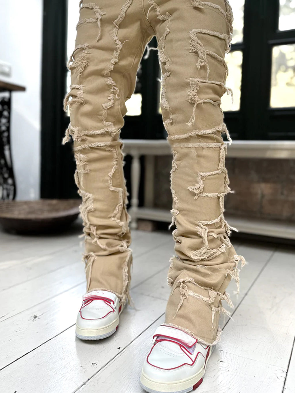 Beige ripped jeans worn with white sneakers on a light wooden floor.