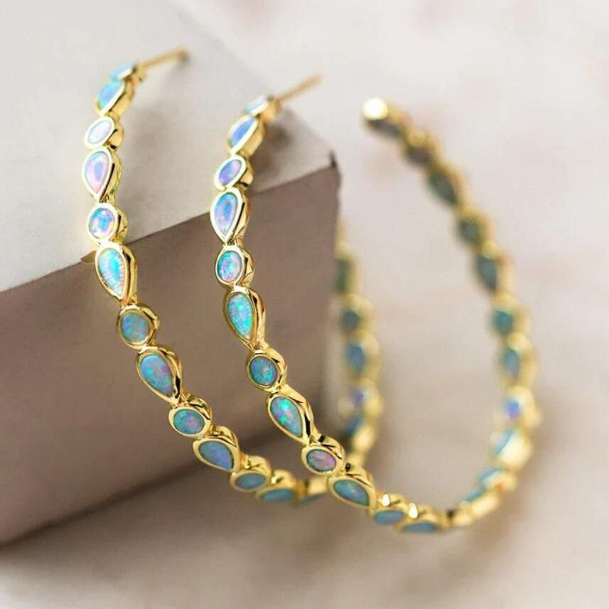 Gold hoop earrings with opal stones on a light background