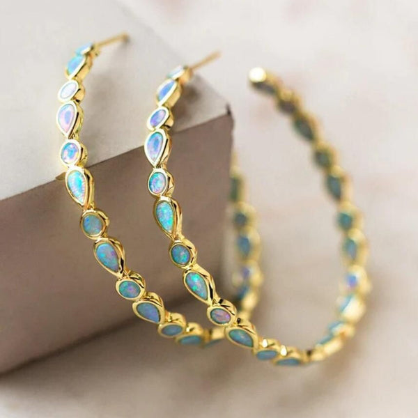 Gold hoop earrings with opal stones on a light background