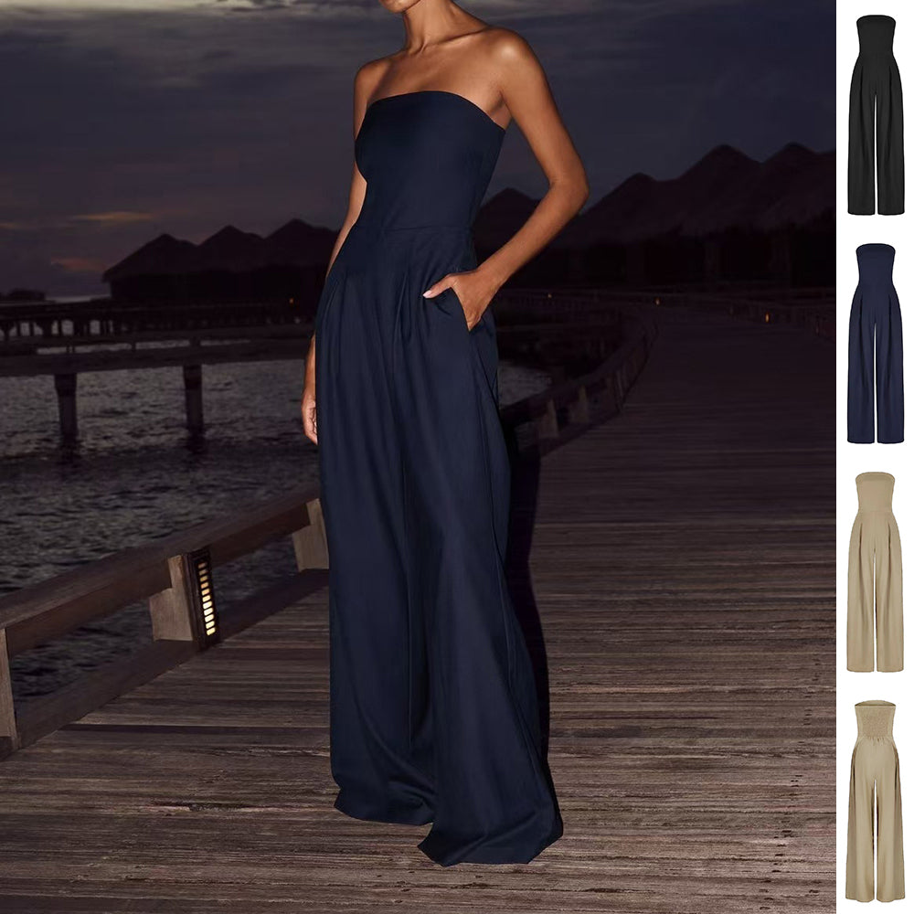 Woman in a navy blue strapless gown standing on a wooden dock with water and sunset background.
