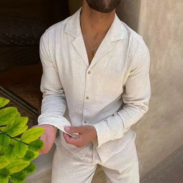 Man wearing a light-colored linen suit standing next to a plant indoors.