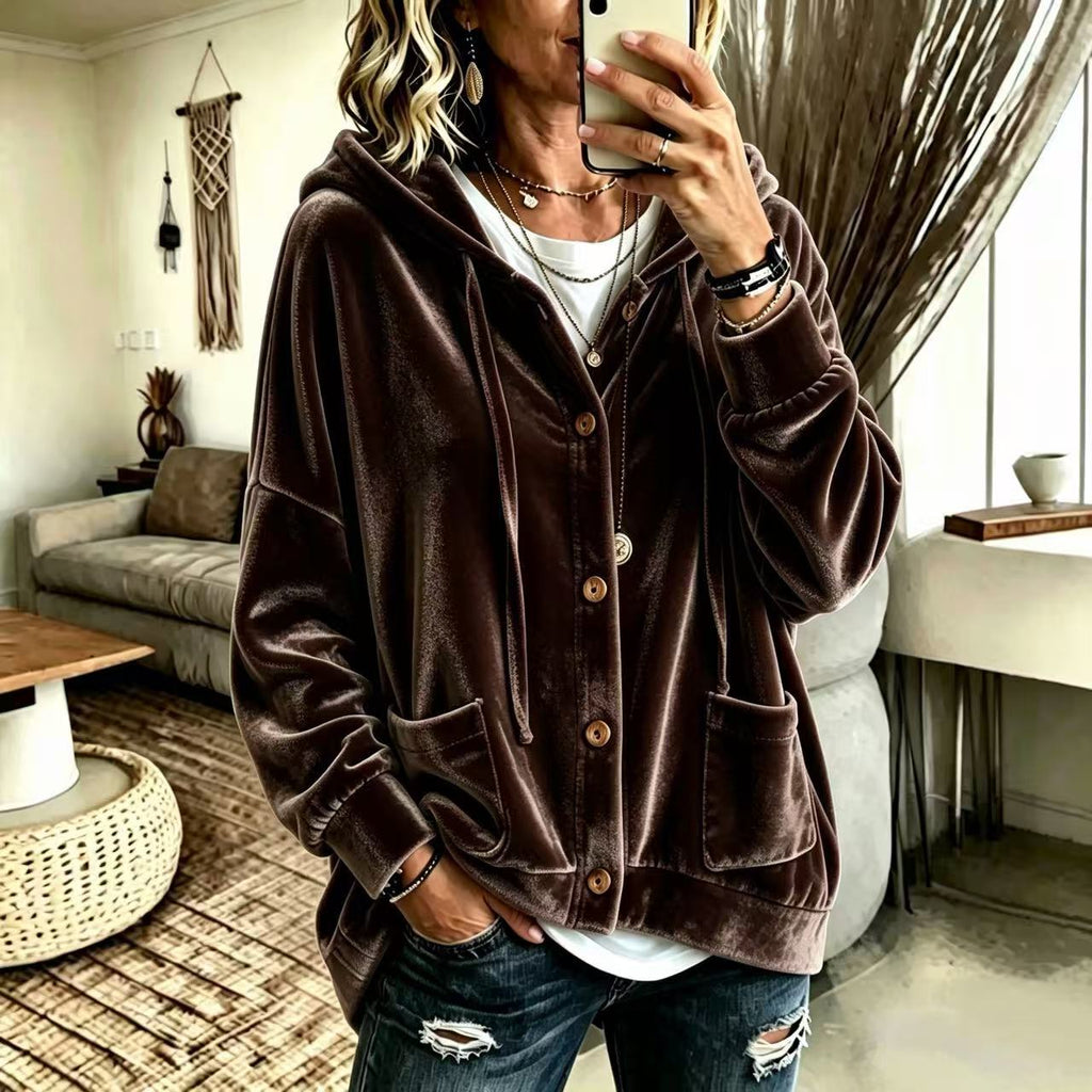 A woman takes a mirror selfie wearing a dark brown velvet button-up hoodie jacket over a white t-shirt and distressed blue jeans in a cozy living room setting.
