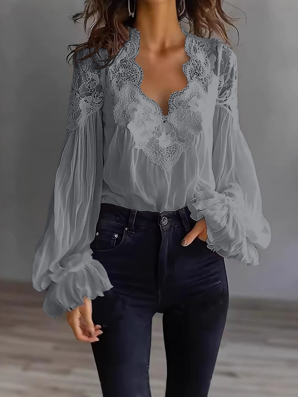 Person wearing a gray lace blouse with long sleeves and dark jeans against a neutral background