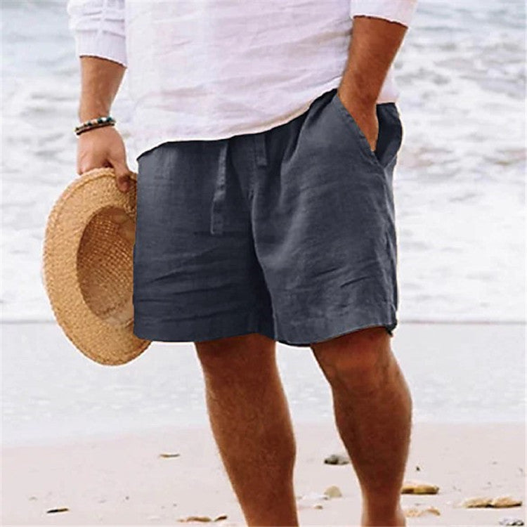 Person wearing gray shorts and holding a straw hat on a beach.