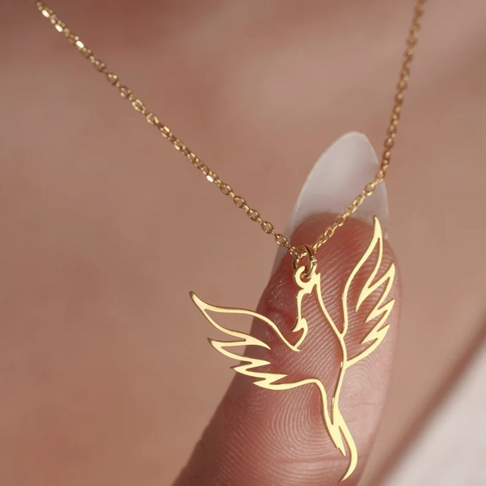 Gold phoenix necklace on a finger against a blurred background